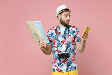 Shocked young traveler tourist man in summer clothes hat using mobile cell phone hold city map...