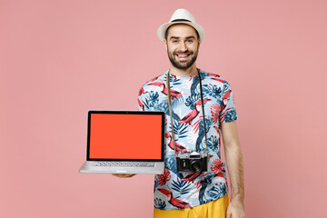 Smiling young traveler tourist man in summer clothes hat hold laptop pc computer with blank empty screen isolated on pink background. Passenger travel on weekends getaway. Air flight journey concept.