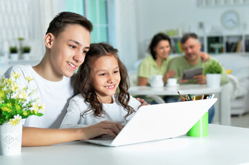 brother and sister using laptop while sitting at table