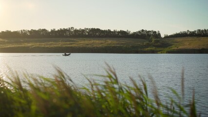 A man rides a motor boat in an inflatable boat on a lake at sunset. Fisherman rides a motor boat on the river.