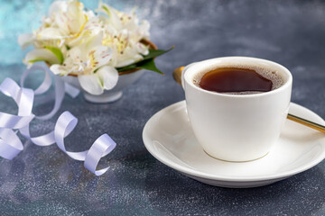 White cup with coffee on a gray background. A bouquet of orchids entwined with a ribbon in the background. Banners, congratulations on the holiday.