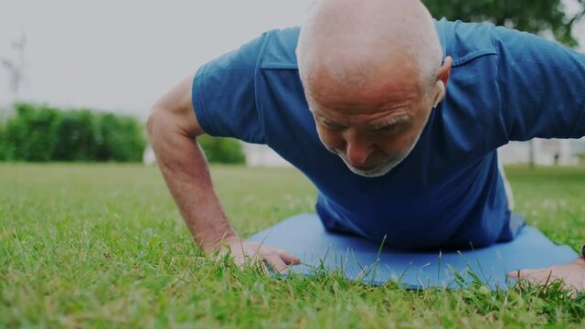 Healthy Sporty Aged Grandfather Makes Push Up Practice while Looking on Smartphone Screen. Watching Live or Video Tutorial Online. Intense Physical Therapy. Slow Motion. Close up.