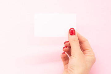Woman's hand with fashionable red manicure holding business card on a pink background . Summer spring nail design.