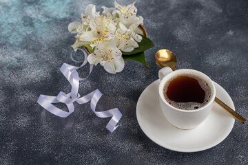 Obraz na płótnie Canvas White cup with coffee on a gray background. A bouquet of orchids entwined with a ribbon in the background. Banners, congratulations on the holiday.
