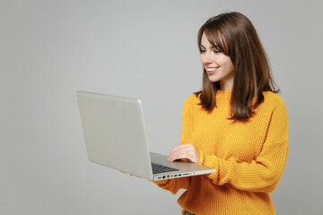 Young smiling happy freelancer copywriter positive attractive caucasian woman 20s wearing casual knitted yellow sweater hold laptop pc computer isolated on grey color background studio portrait