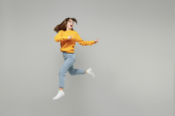 Fototapeta na wymiar Full length side view of young excited overjoyed expressive woman in knitted yellow sweater run fast in air jump high point index finger aside on workspace isolated on grey background studio portrait