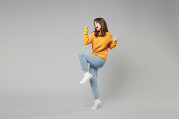 Full length of young smiling positive overjoyed caucasian happy satisfied woman 20s in knitted yellow sweater do winner gesture clench fist looking camera isolated on grey background studio portrait - obrazy, fototapety, plakaty