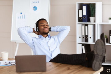 Fototapeta premium Relaxed black man employee listening to music in his office