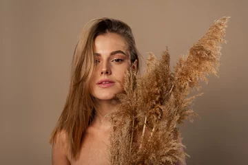 Foto op Plexiglas Close up beauty portrait of an attractive young topless woman with brown hair isolated over beige background, holding dried herb. Skin care concept © etonastenka