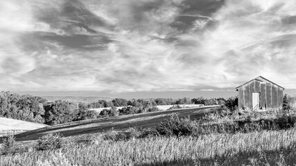 black and white landscape with rolling hills and a barn