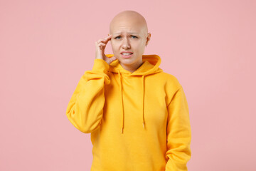 Young bald caucasian troubled pensive worried thoughtful woman 20s without hair in yellow casual sweatshirt shirt put hand on temples touch forehead isolated on pastel pink background studio portrait