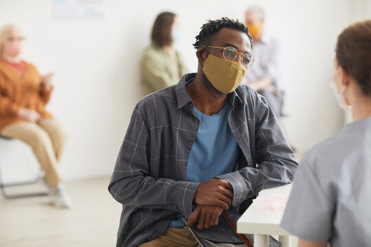 Portrait Of Young African American Man Wearing Mask While Talking To Doctor Or Nurse In ,medical Clinic, Copy Space