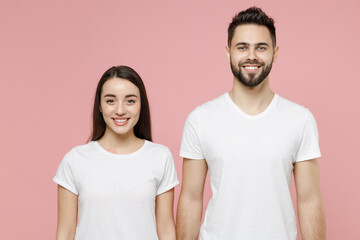 Fototapeta premium Young cheerful couple two friends bearded man brunette woman in white basic blank print design t-shirts posing looking camera standing smiling isolated on pastel pink color background studio portrait.