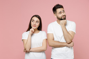 Young pensive couple two friends bearded man brunette woman in white basic blank print design t-shirts thinking dream put hand prop up on chin isolated on pastel pink color background studio portrait.