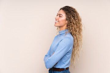 Young blonde woman with curly hair wearing a turtleneck sweater isolated on beige background in lateral position