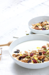 Healthy breakfast: Yogurt with homemade whole grain muesli or granola in a white bowl with honey and coffee on the white table.