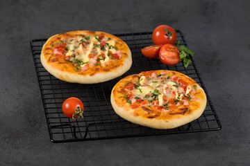 Open pie, Italian pizza with sausage, pickles, tomatoes, mozzarella, greens on a metal stand on a dark gray background
