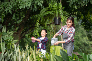 Young Asian mother and daughter happy working in the gardern together on weekend. Daughter helping mother watering.