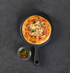 Open round pie, Italian pizza with sausage, pickles, tomatoes, mozzarella, greens on a wooden board on a dark background top view