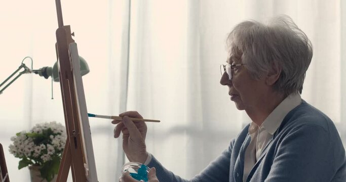 Creative senior lady painting on canvas