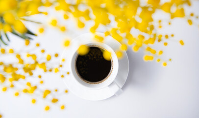 a spring bouquet with yellow mimosa flowers over a cup of black coffee on a white table. concept of 8 March, happy women's day