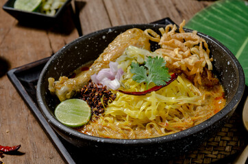 The tasty egg yellow noodle in chicken curry soup with ingredients in the bowl on wooden table. Kao Soi Kai, this is name of the traditional food of northern Thailand..