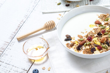 Healthy breakfast: Yogurt with homemade whole grain muesli or granola in a white bowl with honey and coffee on the white table.