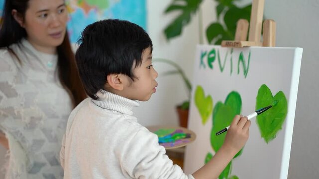 Asian teacher and little child doing painting activities on canvas indoor 