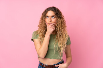 Young blonde woman with curly hair isolated on pink background having doubts and with confuse face expression