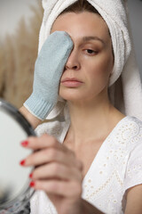 Portrait of a young brunette woman cleaning her face with cosmetic glove in front of mirror