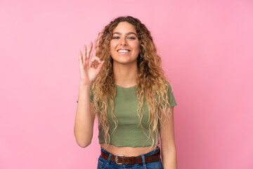 Young blonde woman with curly hair isolated on pink background showing ok sign with fingers