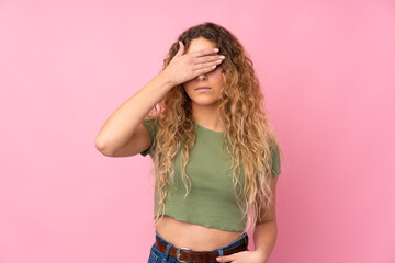 Young blonde woman with curly hair isolated on pink background covering eyes by hands. Do not want to see something