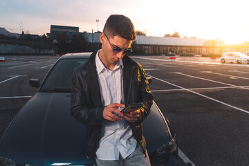Young caucasian man using a smartphone with a sports car behind