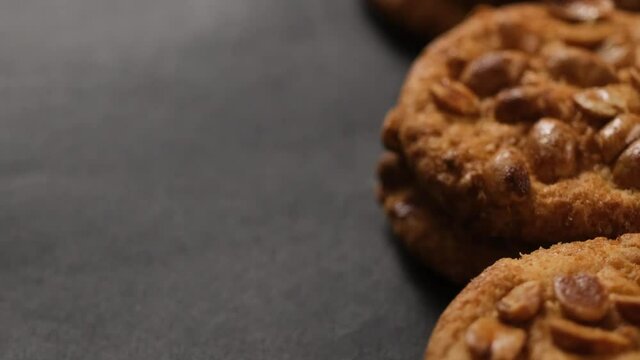 Tasty cookie with fried peanuts lying on dark background, close up view