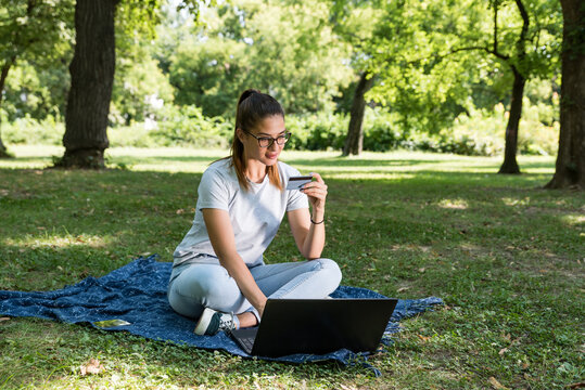 Young college woman sitting in the park taking a break from study and use free time for online shopping on her laptop computer