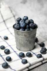 Fresh blueberries in a small metal bucket surrounded with some berries agains concrete background. Side view. Rustic. Vertical