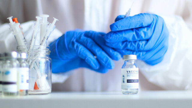 Nurse or doctor in medical protective uniform and latex rubber fill in syringe with medicine from glass vial while preparing for work during coronavirus, flu or measles pandemic for poster, web banner