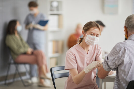 Portrait of young female nurse vaccinating senior man in vaccination center or medical clinic, copy space