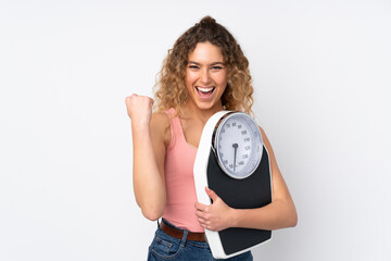 Young blonde woman with curly hair isolated on white background with weighing machine and doing...