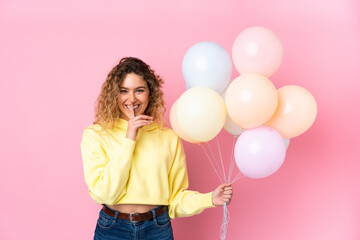 Young blonde woman with curly hair catching many balloons isolated on pink background doing silence...