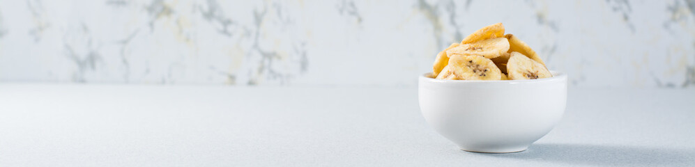 Banana chips in a bowl on the table. Fast food. Copy space. Web banner
