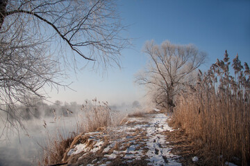 Spring landscape with a river covered with fog, melting snow on the river bank, trees
