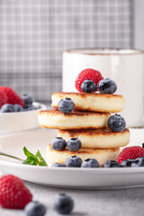 Stack of cheese pancakes with fresh berries, cup of coffee on the table. Tasty breakfast food. Vertical photo - Image