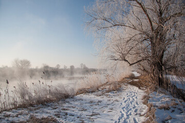Spring landscape with a river covered with fog, melting snow on the river bank, trees