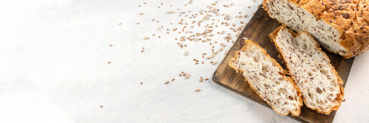 Banner of sliced bread on serving board with flax and sunflower seeds. Fresh, tasty, round wheat bread with flax seeds on a white textured table with space for text. Copy space.