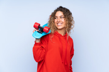 Young blonde woman with curly hair isolated on blue background with a skate with happy expression