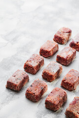 Composition with raw square cutlets on light background. Natural food for dogs. BARF dog diet