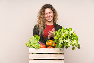 Farmer with freshly picked vegetables in a box isolated on beige background applauding