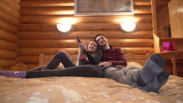 Romantic Young Couple Lying In Bed Enjoying A Relaxing Cuddle While Watching TV