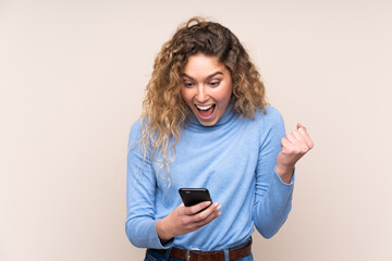 Fototapeta premium Young blonde woman with curly hair wearing a turtleneck sweater isolated on beige background surprised and sending a message